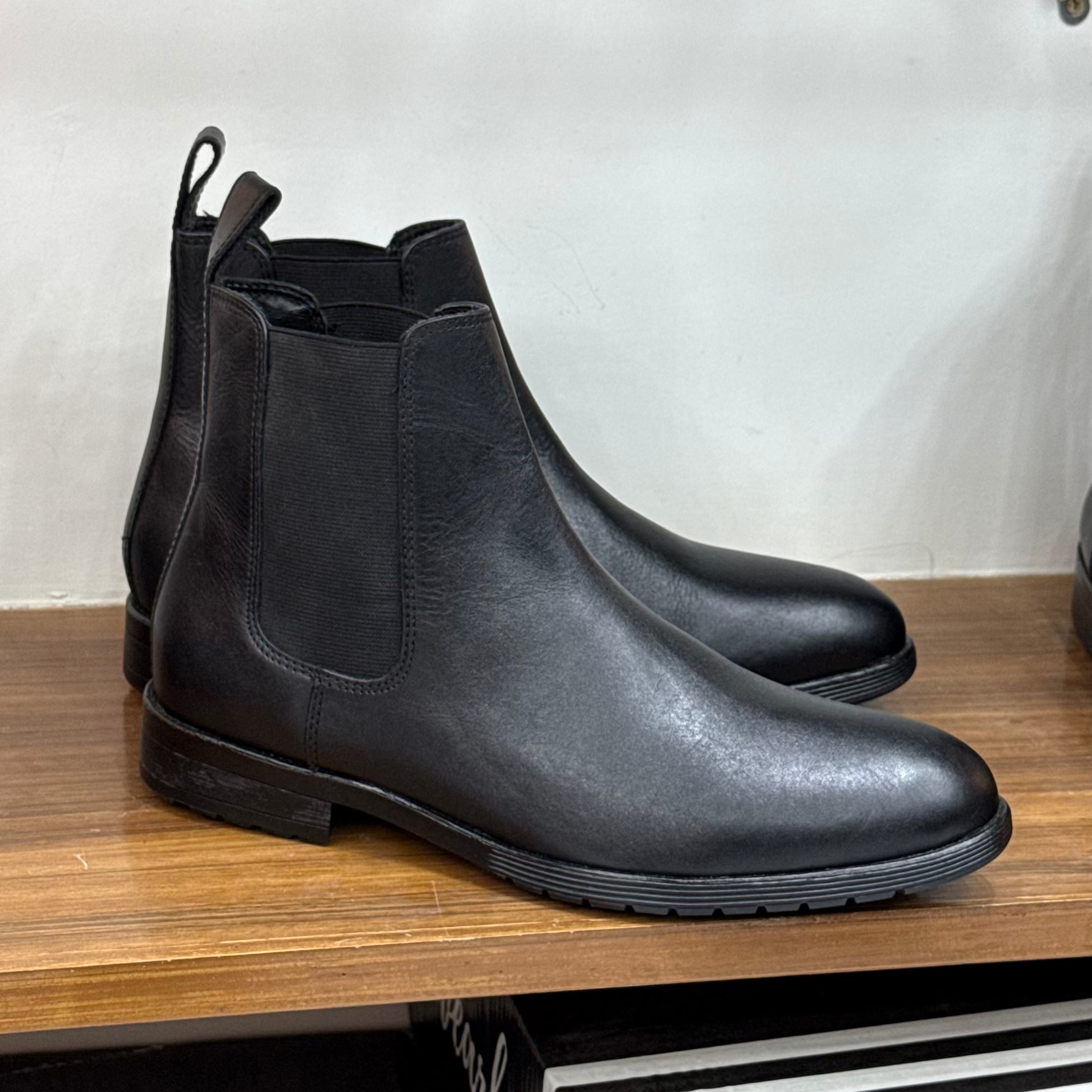 Pair of black leather Chelsea boots on a wooden surface with a white background